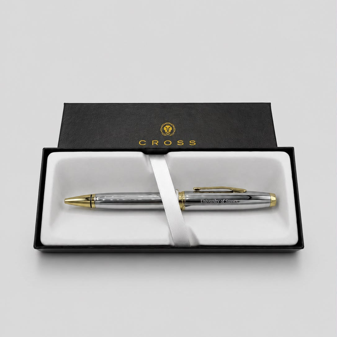 A silver and gold Cross pen presented in an open black gift box with a white insert and ribbon, photographed on a light gray background.