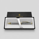 A silver and gold Cross pen presented in an open black gift box with a white insert and ribbon, photographed on a light gray background.