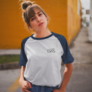 Woman wearing a white and black baseball shirt with a graphic design, standing against a yellow wall.