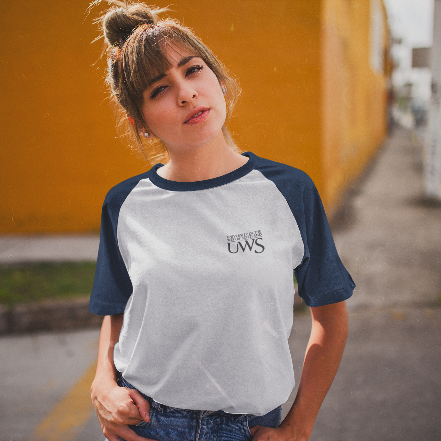 Woman wearing a white and black baseball shirt with a graphic design, standing against a yellow wall.